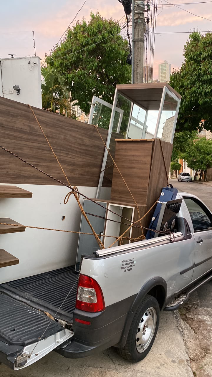 Caçamba da Strada prata com móveis planejados em pé, um eletrodoméstico e várias cordas cruzadas e amarradas prendendo a carga