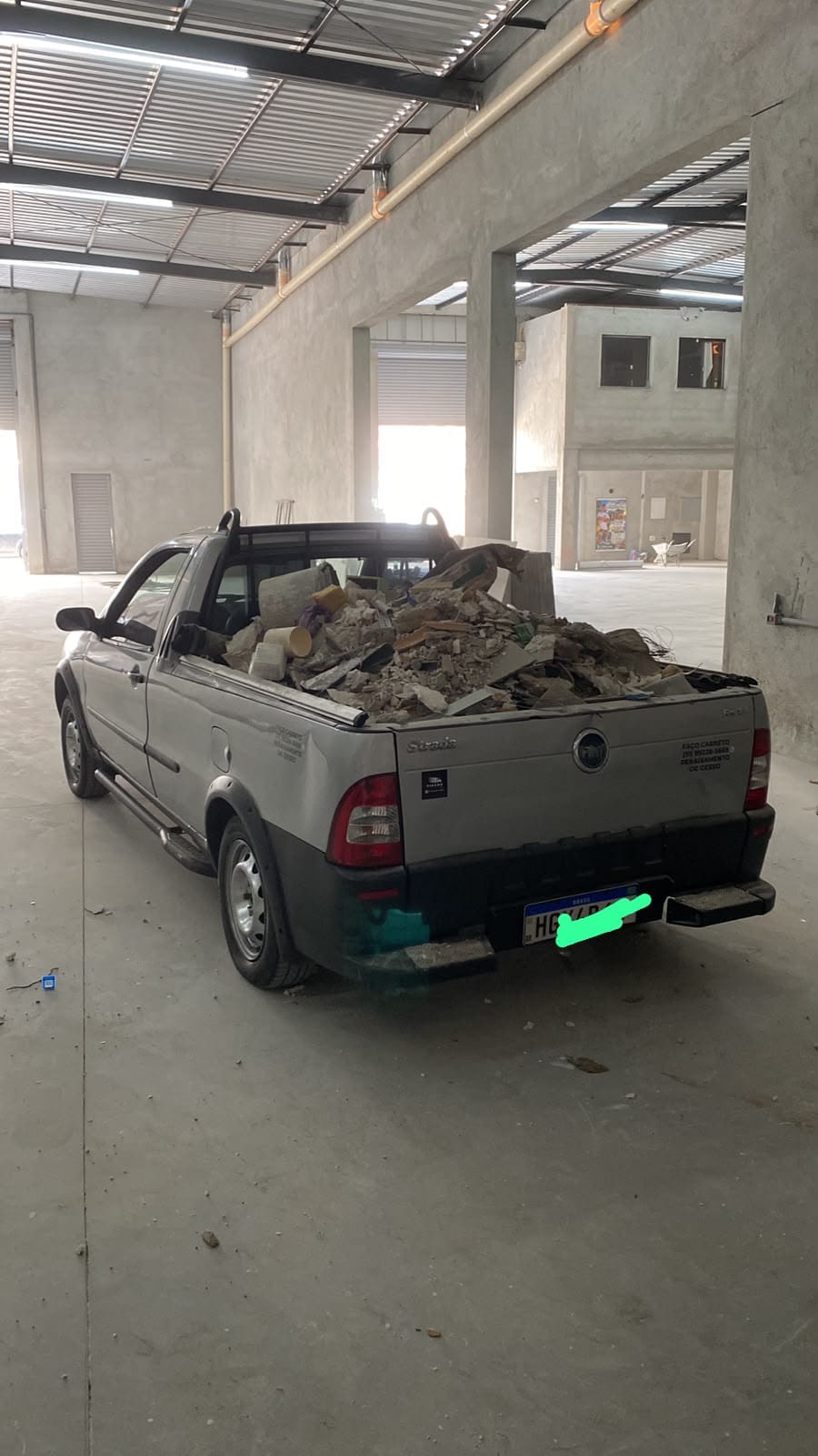 Strada prata de traseira com a caçamba cheia de entulho de obra, dentro de um galpão